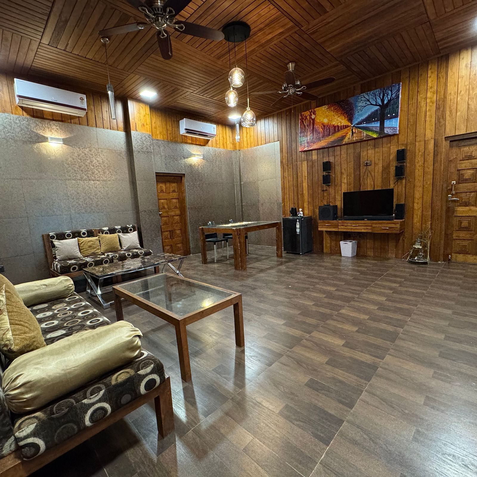 A living room with wooden paneling, a fan on the ceiling, a patterned sofa, and a wooden table, under warm lighting.