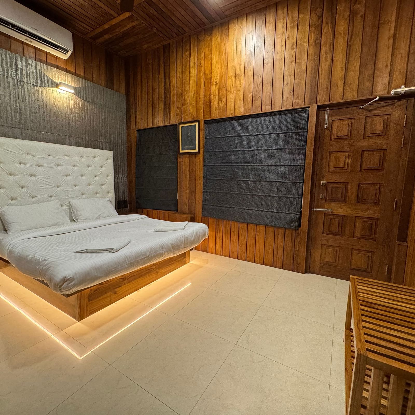 A bedroom with a modern platform bed with illuminated base, a white tufted headboard, and wooden paneling on the walls.