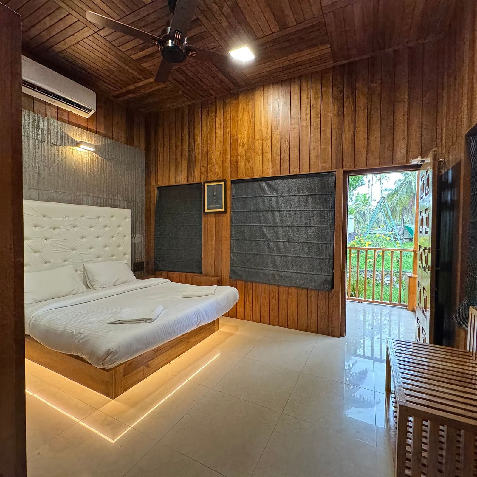 A bedroom with a modern platform bed with illuminated base, a white tufted headboard, and wooden paneling on the walls.