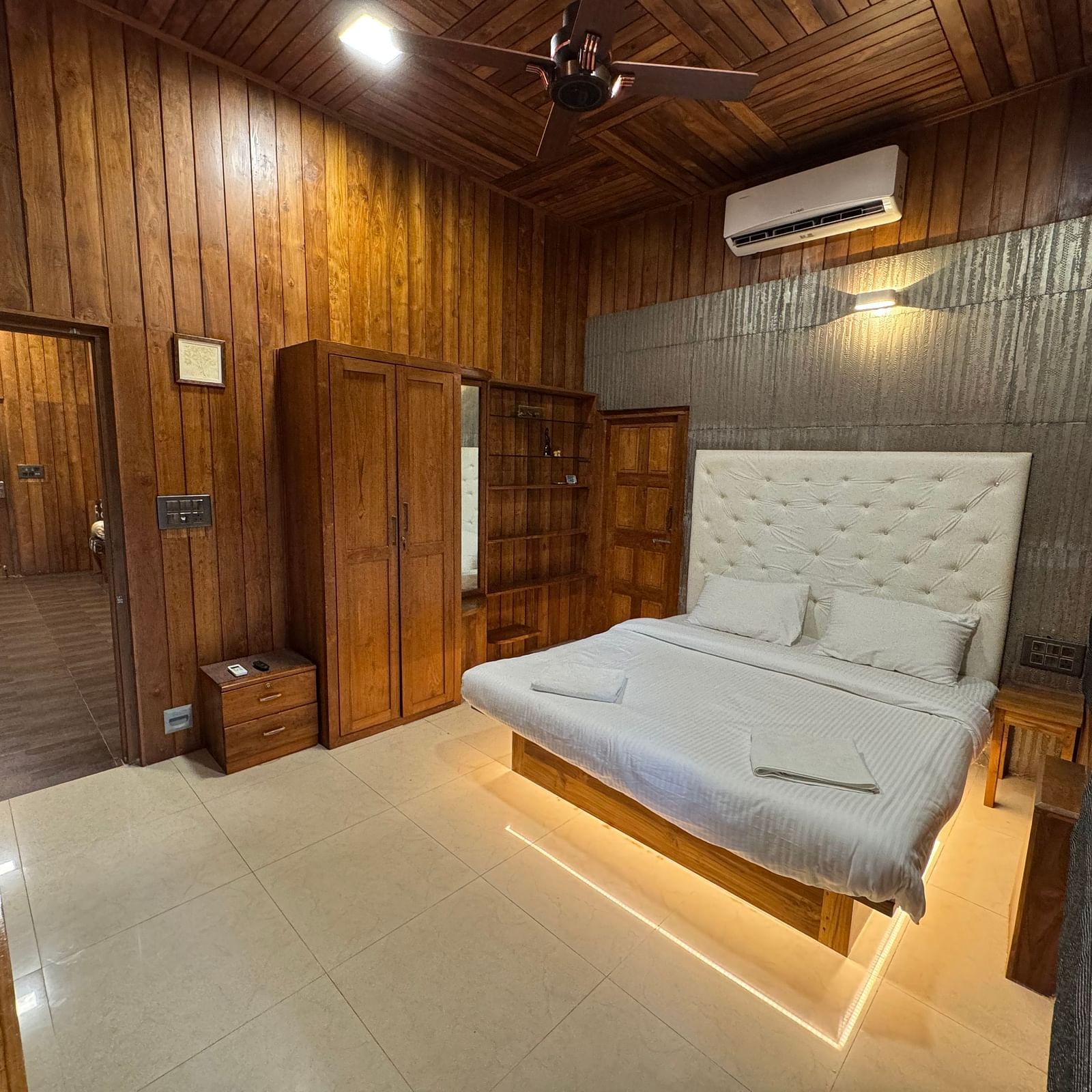 A bedroom with rich wooden walls and ceiling, a platform bed with a white tufted headboard, and a ceiling fan.
