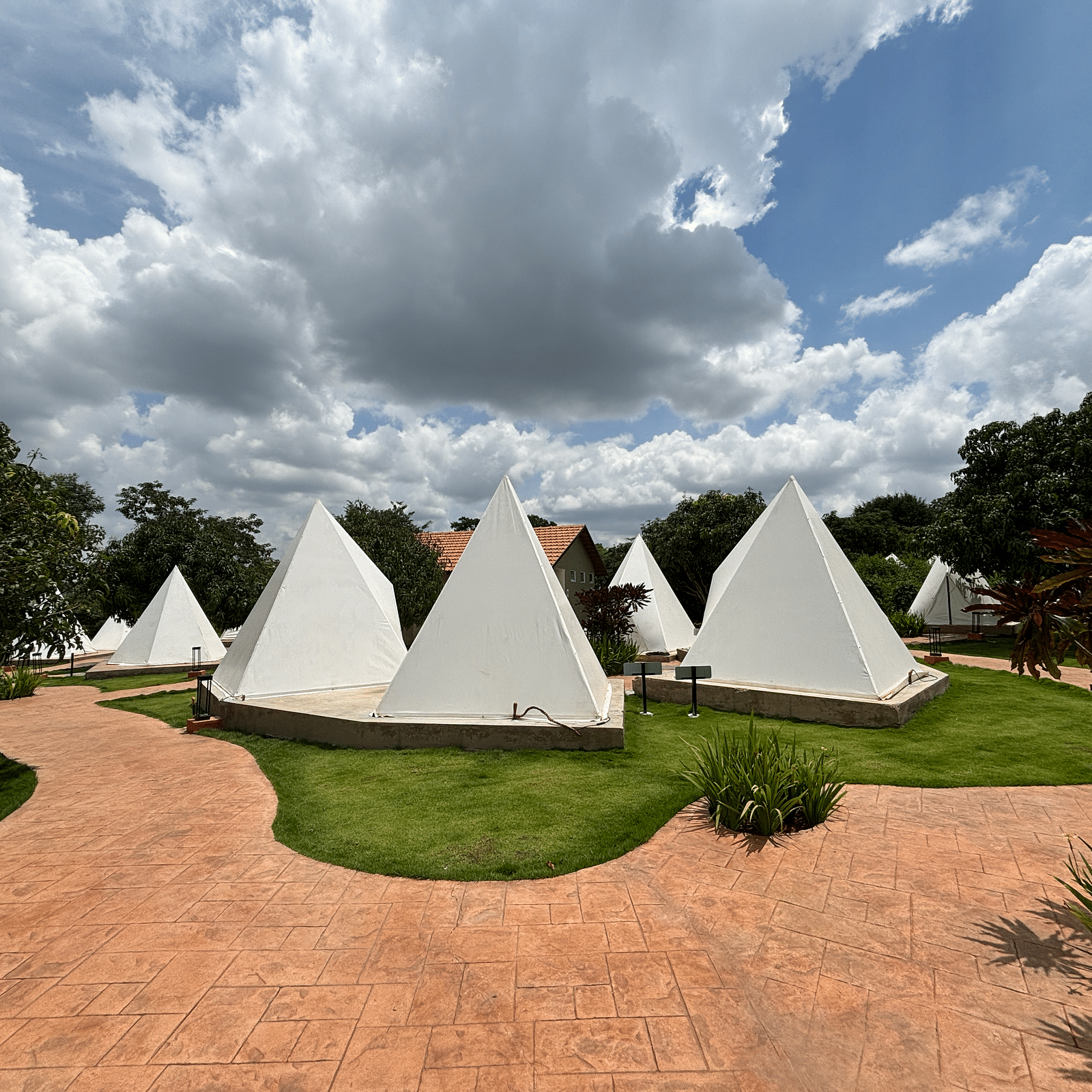 A scenic view of a resort area with tents lined along a neat walkway, surrounded by a well-maintained lawn.