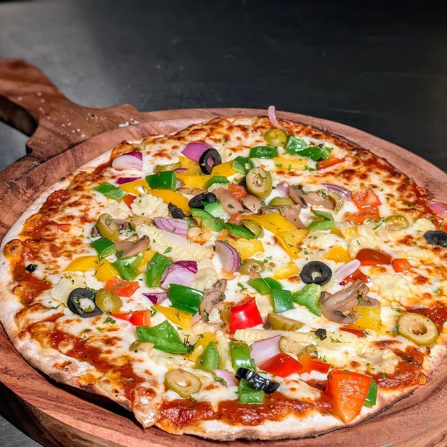 A close up of pizza with loaded veggies, placed on a wooden pizza plate.