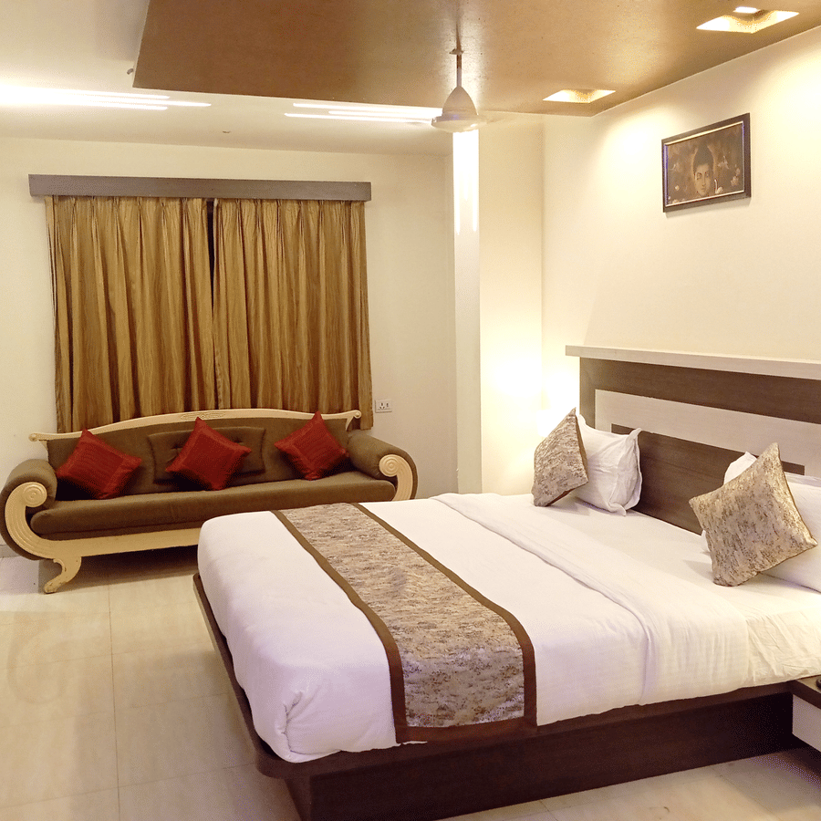 Well-furnished suite room showcasing a double bed, a wooden sofa with red cushions, and a small side table.