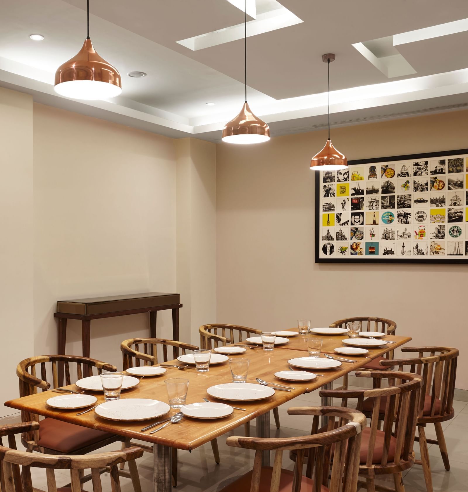 The private dining area at Monday Hotels Mahape, Navi Mumbai, with a long wooden table and decorative wall frames.
