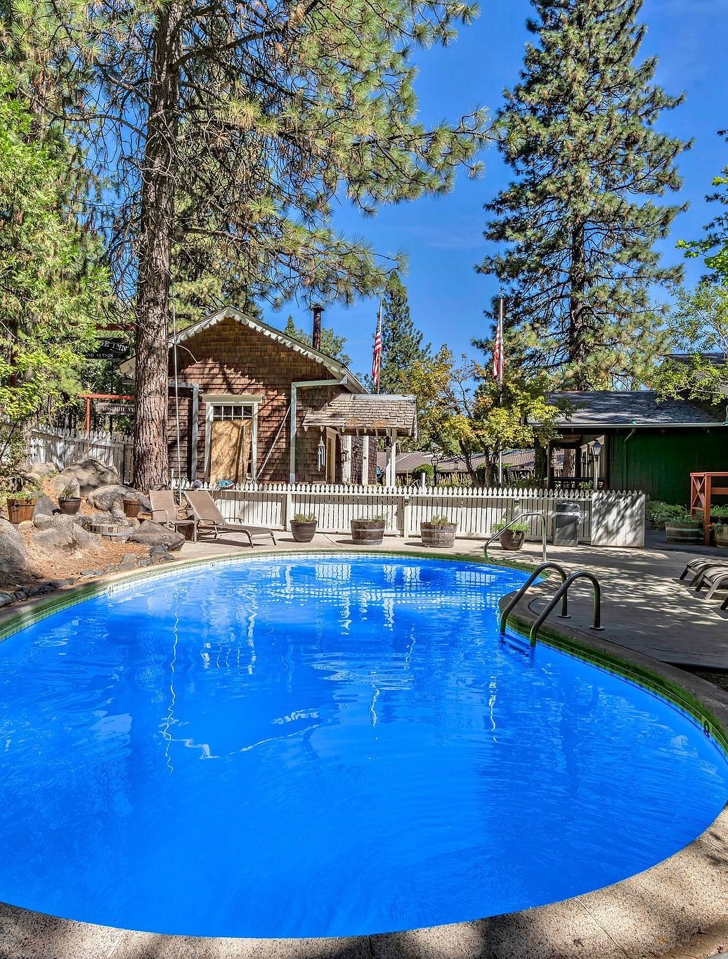 A view of the outdoor swimming pool with a cabin in the backdrop surrounded by trees on a clear blue day