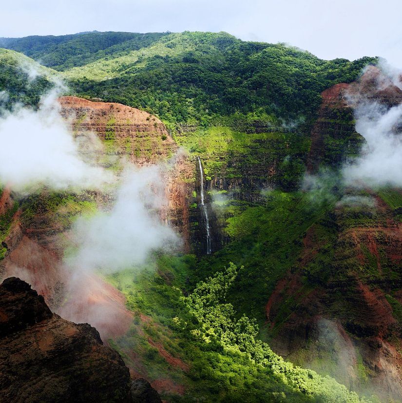 Scenic view of a lush green valley with waterfalls and mist-covered hills in a tropical landscape.