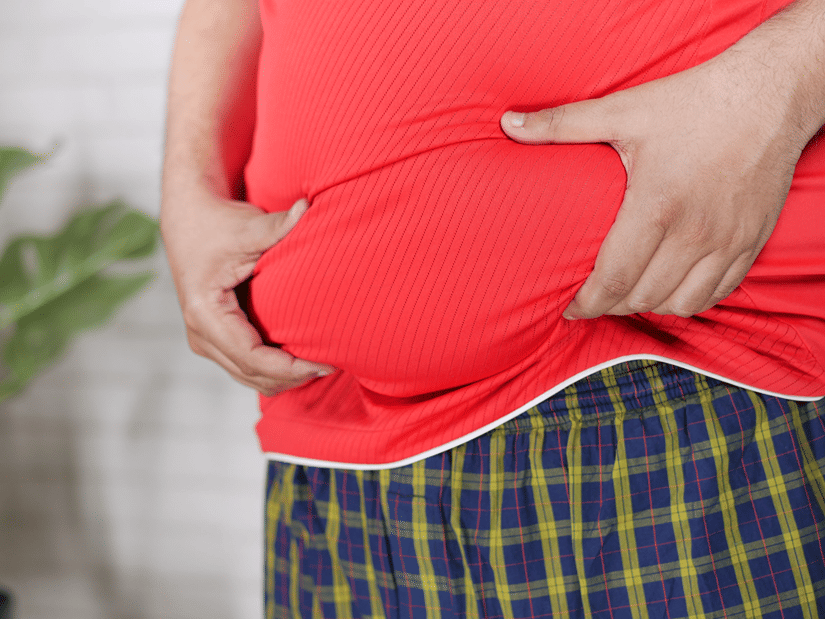 A person in a red T-shirt holding excess fat around the stomach