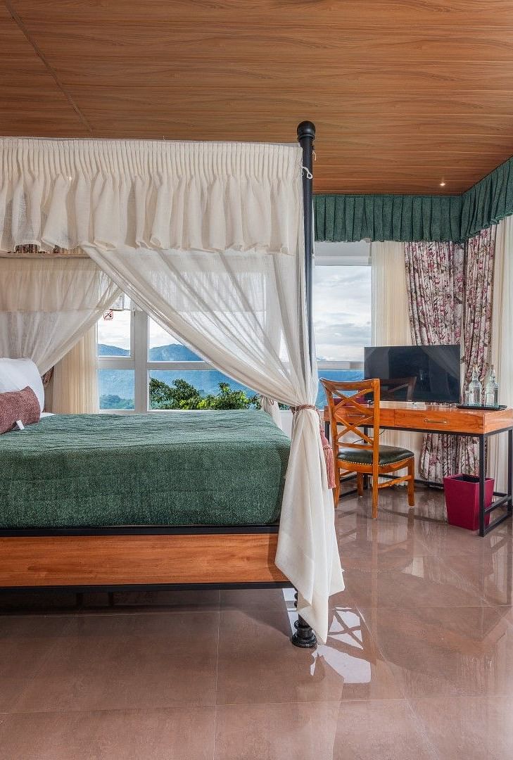  A generously sized bed with curtains on the sides, accompanied by wooden furniture and a breathtaking mountain view through the large windows.