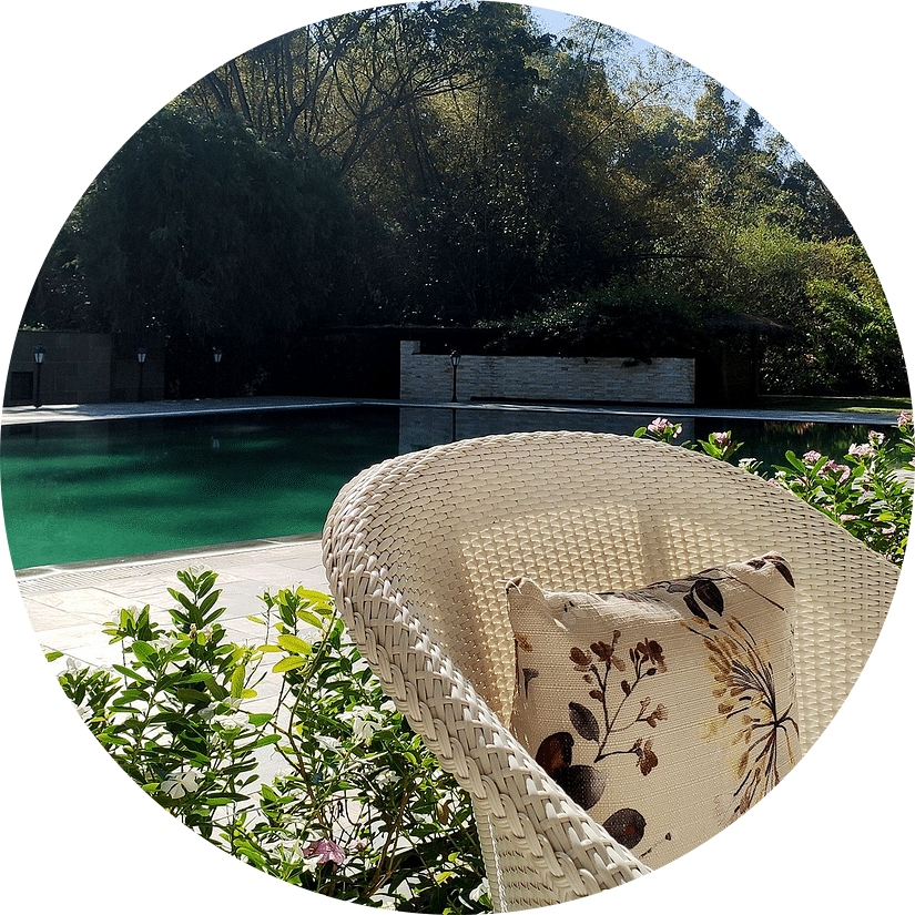Close up image of an elegant chair a pool with greenery providing shade on the pool on the background at Amanvana Spa Resort, Coorg - Luxury Resort