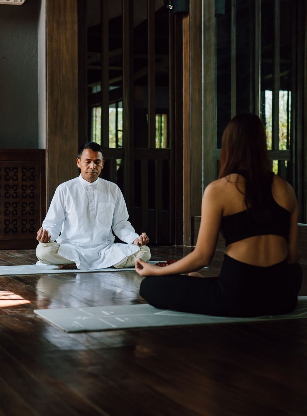 A man in white attire teaching a woman meditation indoors.