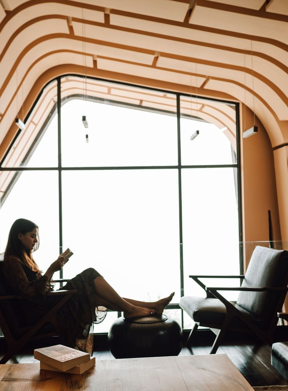 Person reading a book in a stylish, cozy room with unique arched ceiling design.