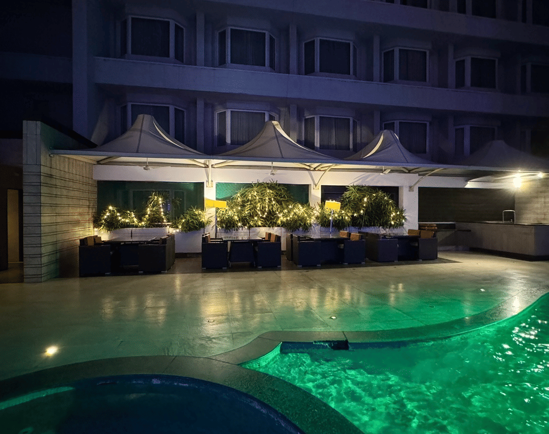 A nighttime view of an outdoor lounge area with canopy umbrellas, plants, and a glow-in-the-dark green swimming pool - Cenneys Gateway