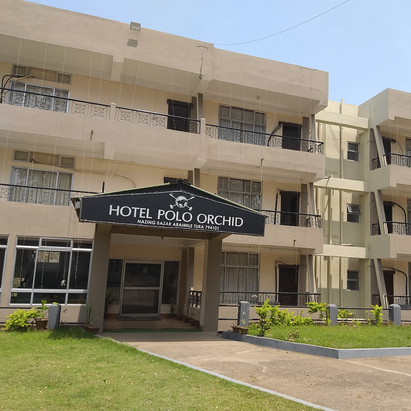 Hotel Polo Orchid facade with its sign, a neat lawn in front, and clear skies above.