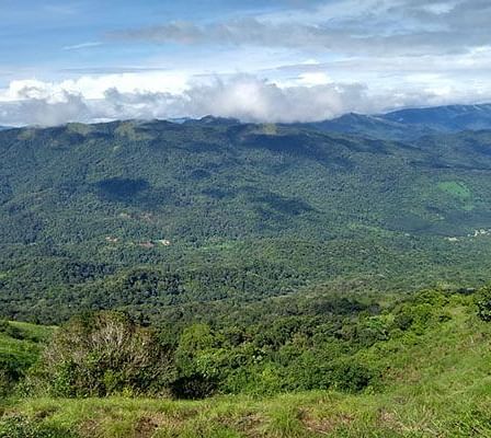 A lush, green mountainous landscape under a cloudy sky, showcasing the natural beauty of a hilly region.