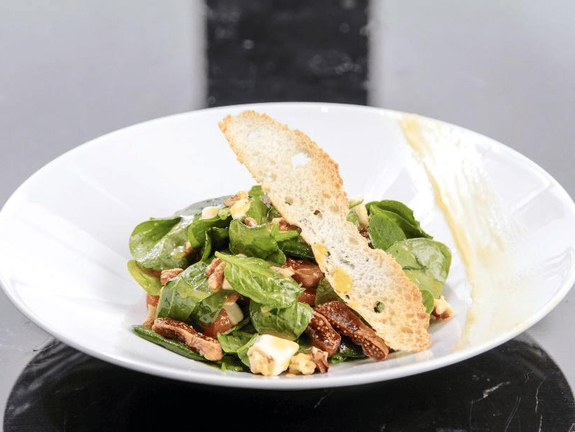 A gourmet spinach salad with bacon, feta, and a slice of toasted bread, elegantly presented on a white plate at YO1 Longevity & Health Resorts, Catskills