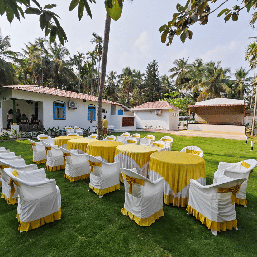 Tables and chairs arranged in the wedding lawn with trees in the backdrop at Ibex Resorts, Coimbatore (Kakarla).