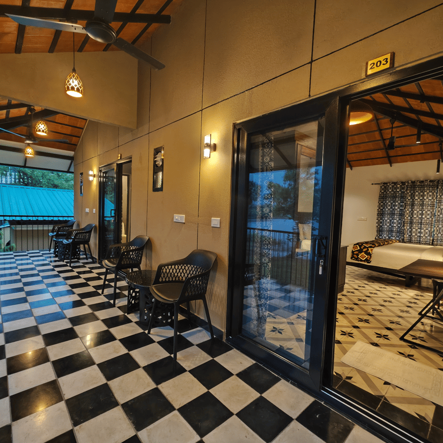 Exterior corridor with checker tiles leading to glass-door to guest rooms under a warm-lit canopy - Ibex Resorts, Malampuzha (Kava Eco Camp and Caravan Park)