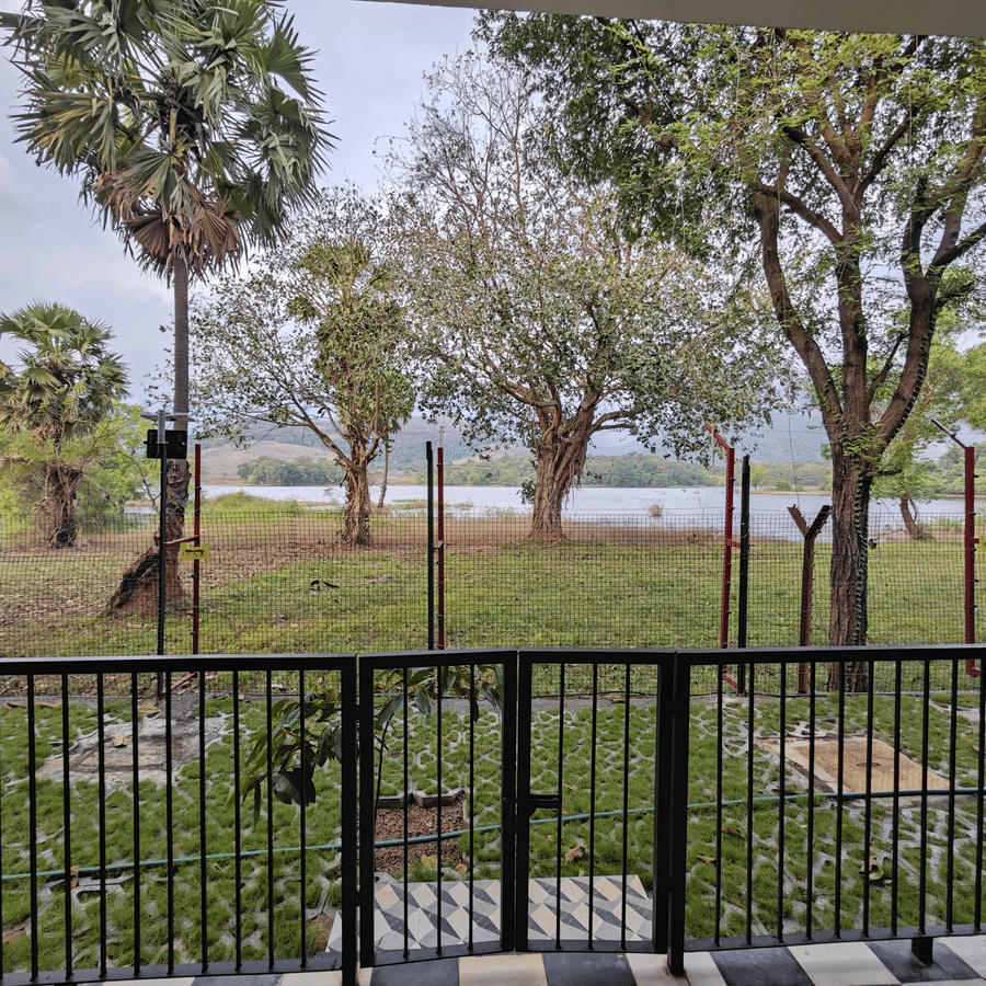 View from a resort balcony overlooking a green lawn, palm trees, and the waterfront - Ibex Resorts, Malampuzha (Kava Eco Camp and Caravan Park)