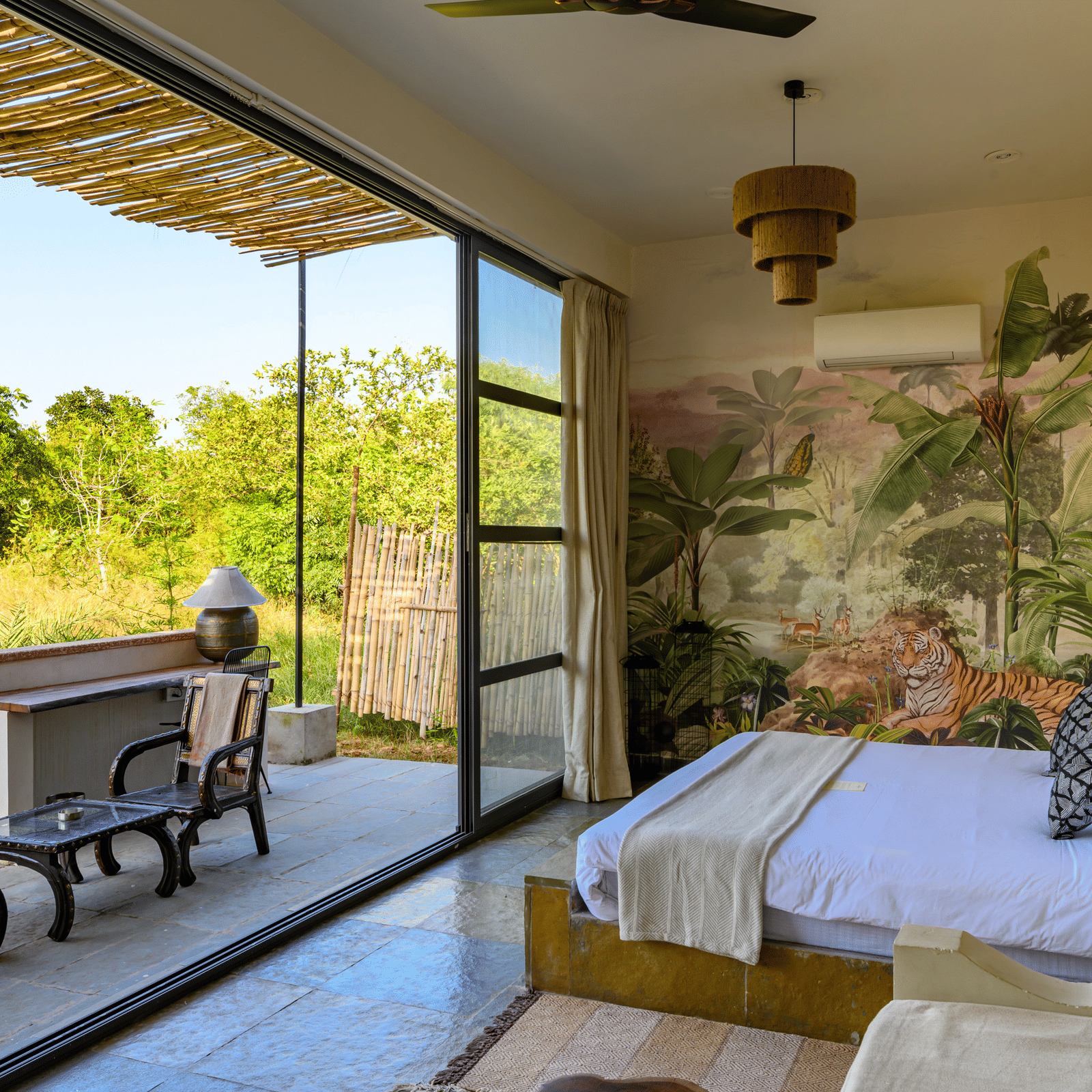 An image of a room with a queen size bed and decorative items with wall hangings and an expansive glass door with an outdoor seating arrangement - Utsav Camp Sariska