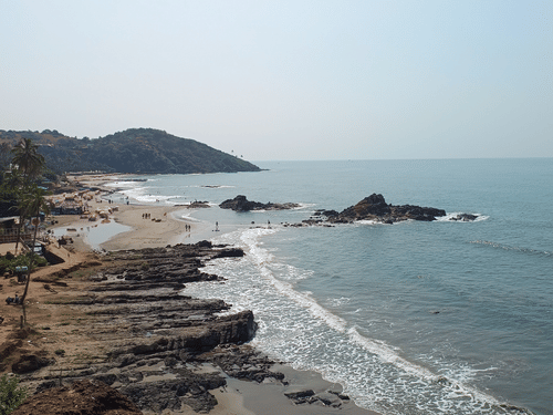 Wide view of Anjuna Beach with waves reaching sandy shores of Goan coastline.