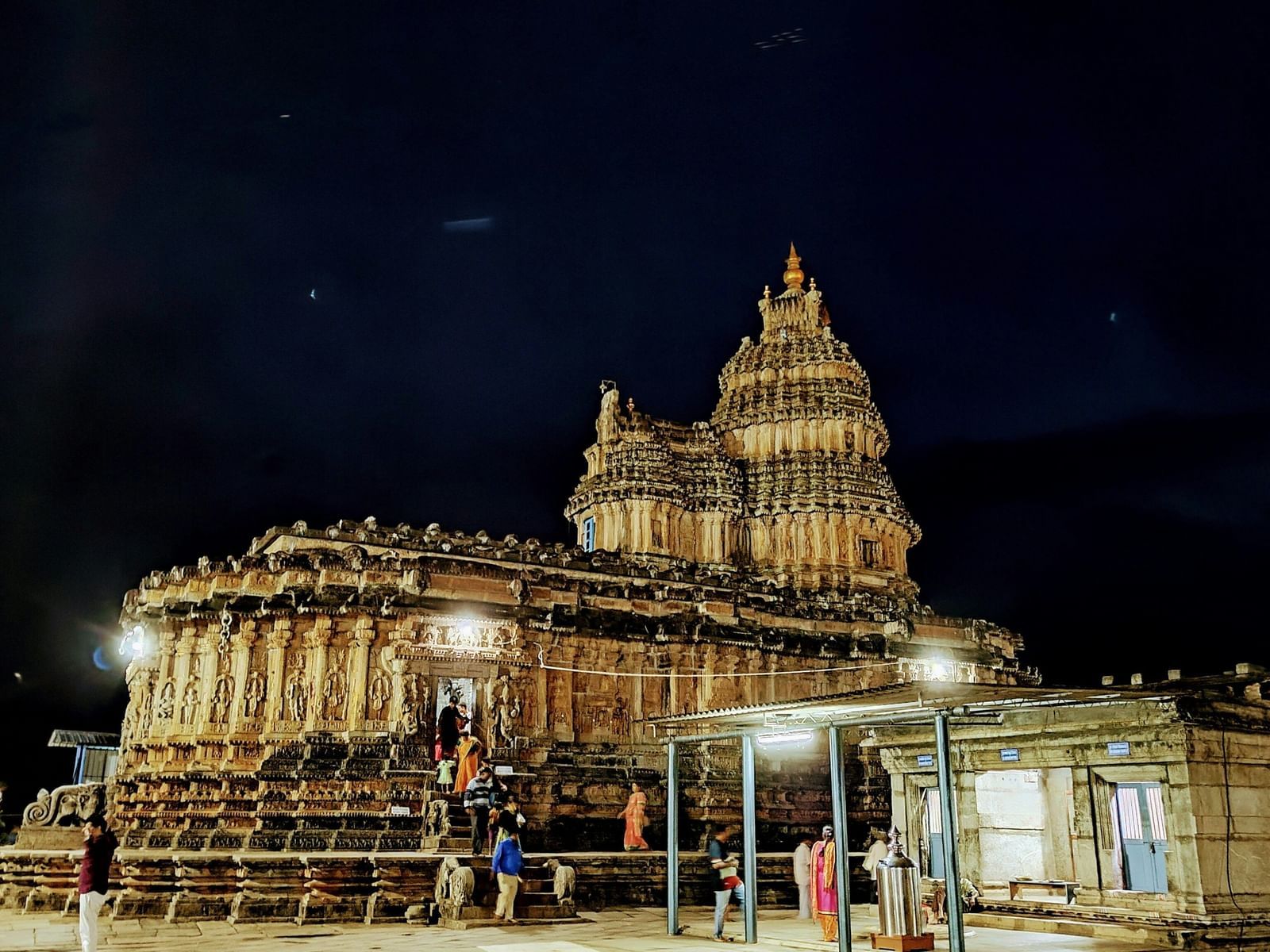  A nighttime shot of an ancient stone temple with a tiered tower, lit up against a dark sky, with people gathered in the foreground.