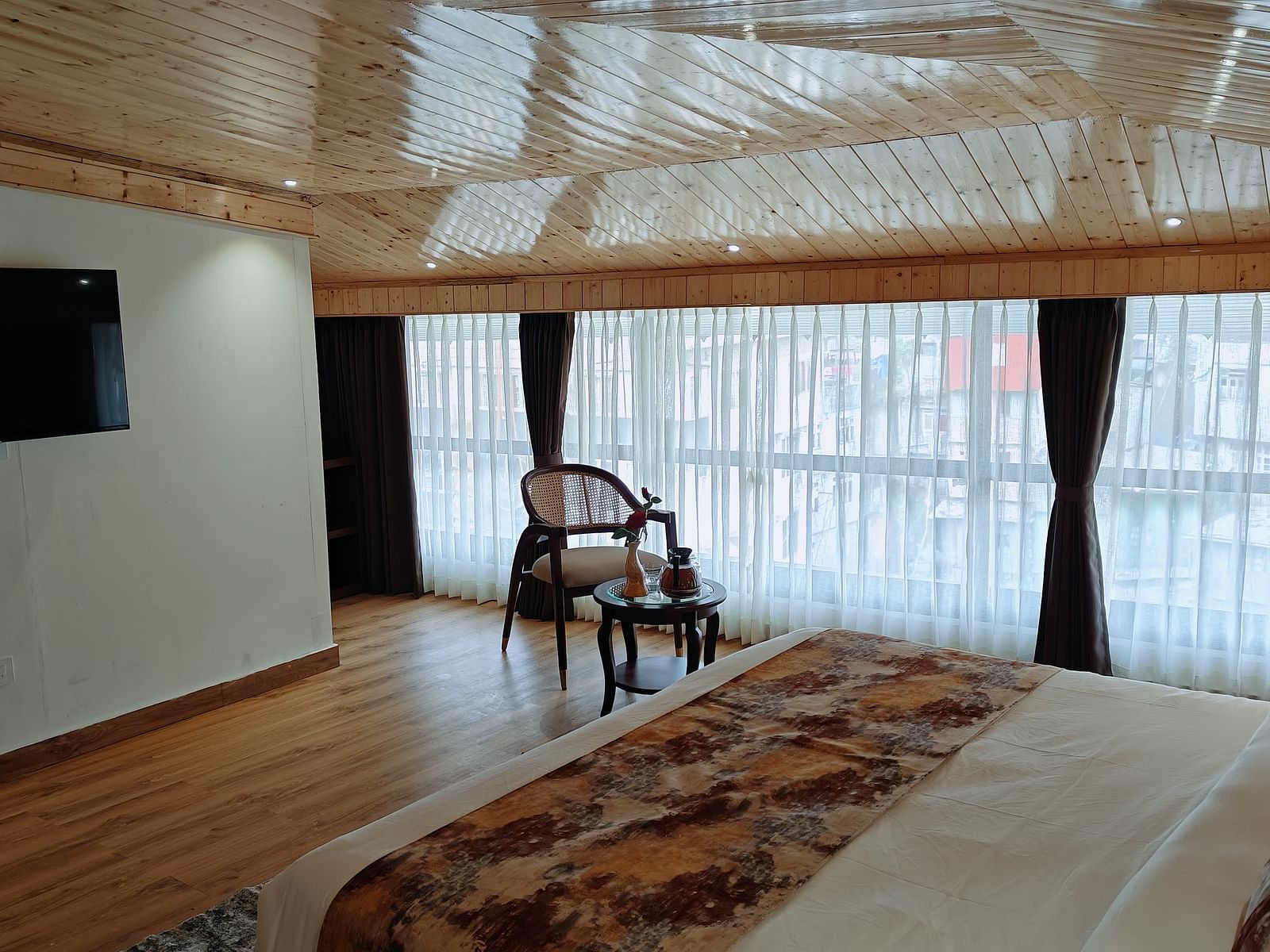 A hotel room with a tv mounted on the wall, a chair, and a decorative runner on the bed - Sumitel JB Park, hotel in Darjeeling