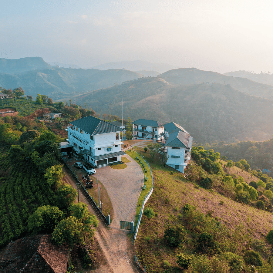An aerial view of the hotel on a grassy hilltop surrounded by tea plantations and rolling mountains | Abad Silvermist, Vagamon