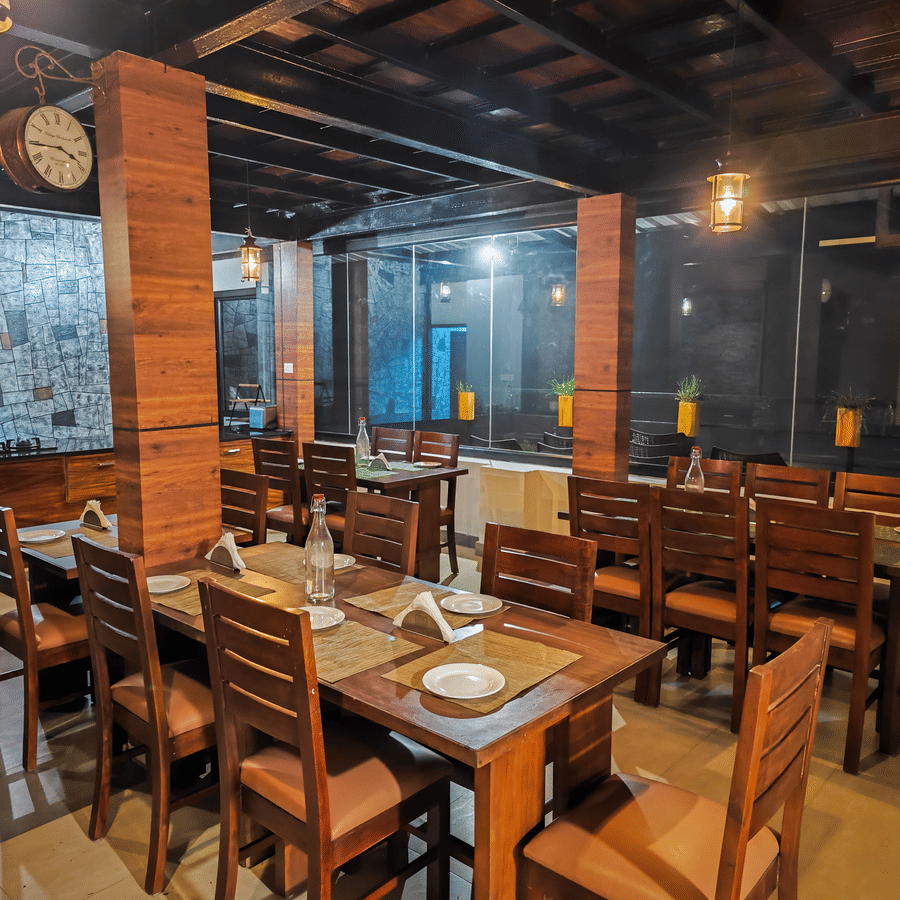 Well lit dining hall at Ibex Resorts Valparai Tale Rock showcasing handcrafted wooden tables brick pillars and ambient lighting providing guests with a warm and welcoming setting amidst the scenic surroundings of Valparai.