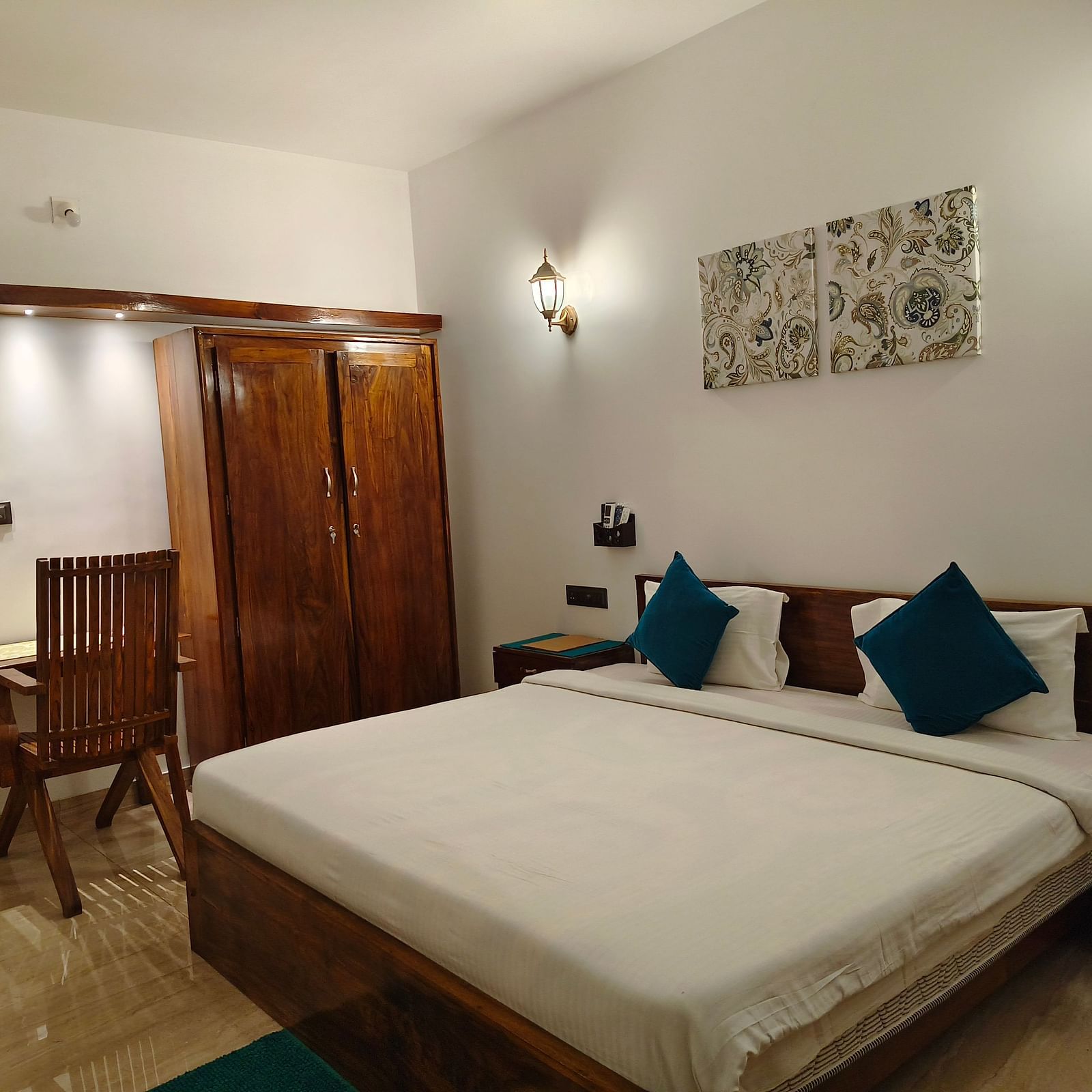 Wide view of a double bed with blue pillows, a chair and a cupboard in 102 room at Ananda Holiday Home, Wayanad 9