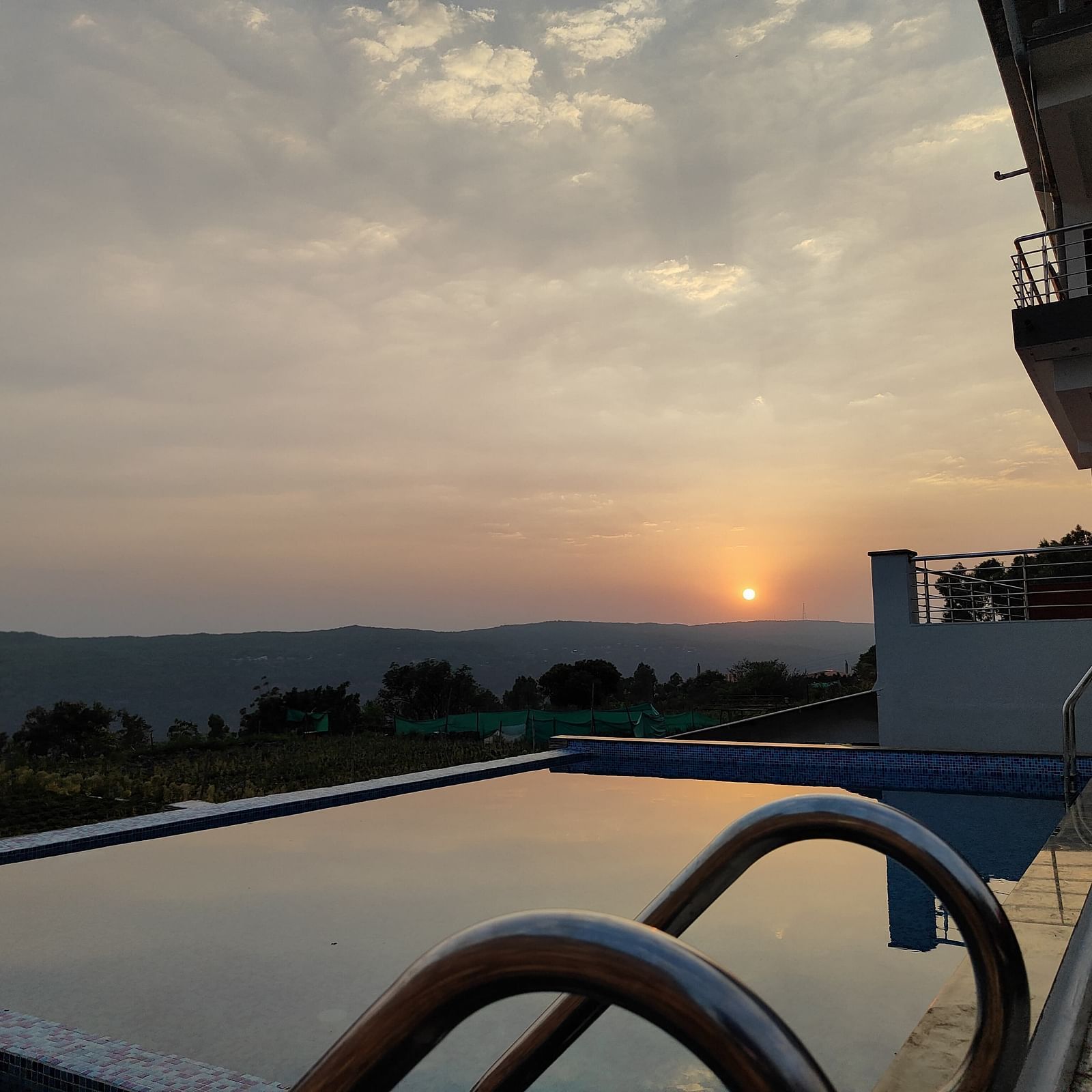 A view of the swimming pool overlooking the sunset surrounded by hills.