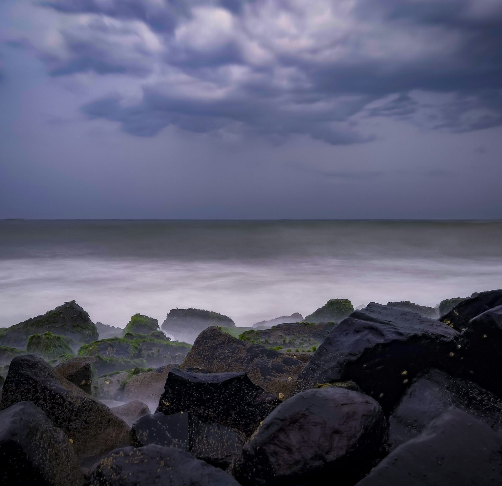 An overview of promenade beach with clouds hovering over and rocks in view as well