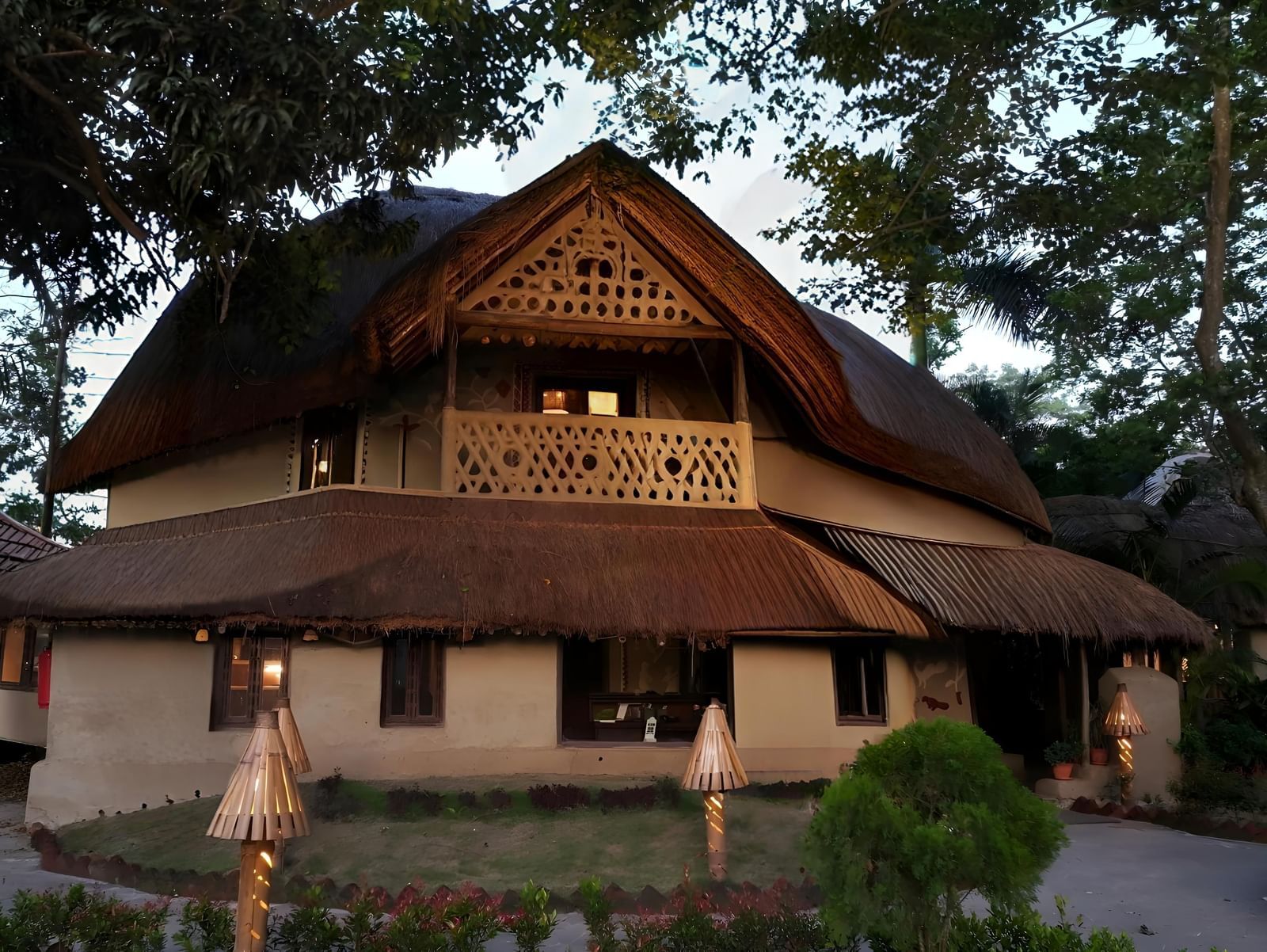 A traditional wooden house with a tiled roof is situated amidst lush greenery | Vedic Village Spa Resort, Kolkata