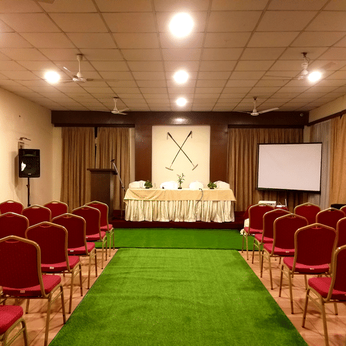 A conference room with rows of red chairs, a podium, and a projection screen.