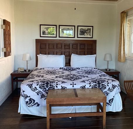 Bedroom with a large bed, ceiling fan, table, chair, and framed art on the wall | A Stone's Throw Away