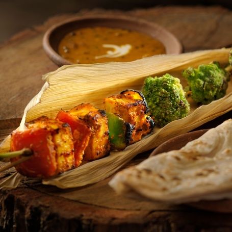 Paneer tikka skewer, broccoli, naan and dal on wood.