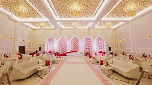 A luxurious wedding hall with elegant chandeliers, white and gold decor, and soft pink lighting highlighting an aisle lined with plush sofas. The setting is opulent and designed for an extravagant event - La Maison Hotel, Doha