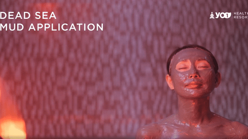 Woman enjoying a Dead Sea mud application treatment, her face and body covered in therapeutic mud at YO1 Longevity & Health Resorts