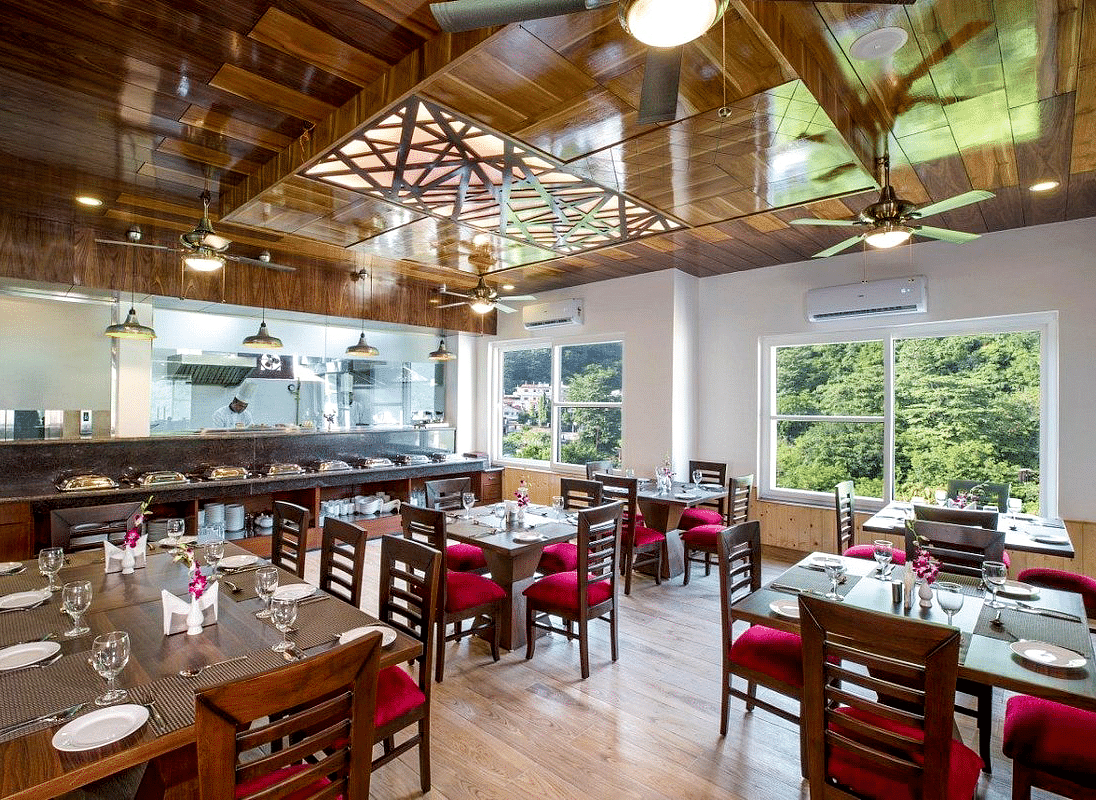 Full view shot of the restaurant at Regenta Inn DLS with neatly arranged dining tables with ample of natural lighting inside.