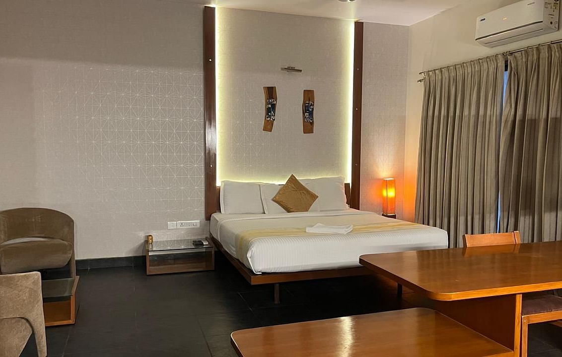 Modern hotel room with a platform bed featuring a white duvet and decorative pillows, a wooden desk with a chair, and a soft armchair - Astra Hotels & Suites, Spice Garden Layout