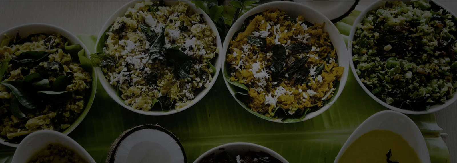 A close-up, overhead shot of multiple small white bowls filled with different green and yellow Indian curries and side dishes.