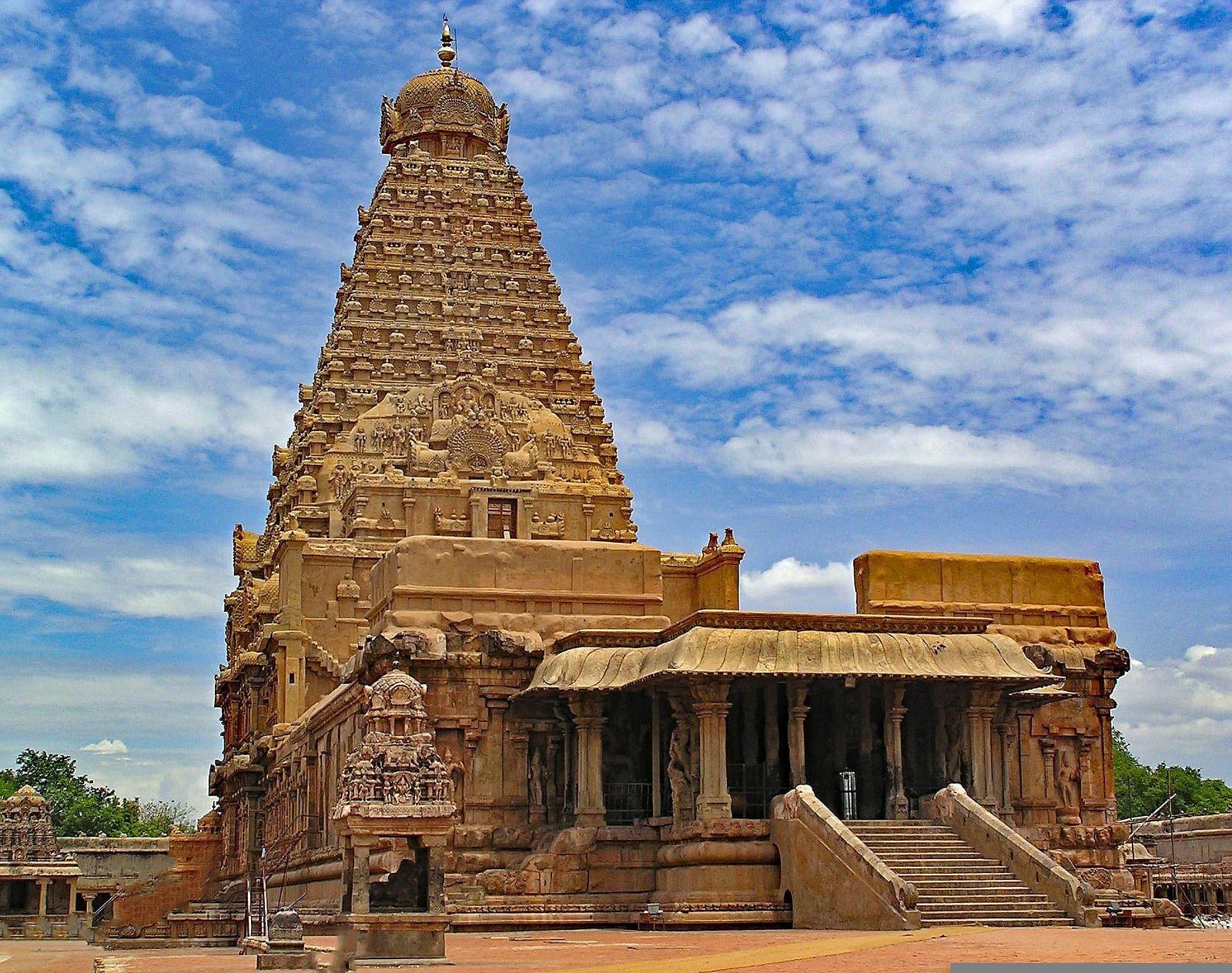 A far out view of an ancient temple with a cone roof and a a building in front of it.