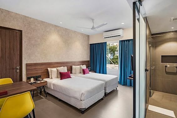 One of our rooms in thoothukudi with twin beds, a table with yellow chairs, and a modern shower area in front - Regency Tuticorin by GRT Hotels