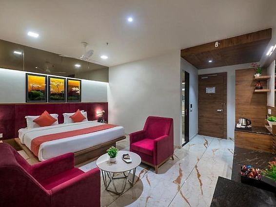 A room featuring a neatly made bed, a seating area, and a dressing table at Angel Lords Eco Inn Amreli.