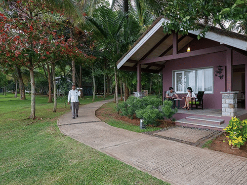 Waterfront Villa at The Serai Kabini featuring a staff member walking on the pathway surrounded by verdant manicured lawn and a couple of guests on the patio