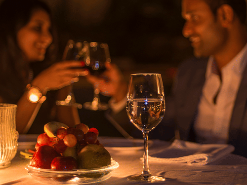 a couple toasting their wine glasses on their romantic candlelight dinner at The Serai, Chikmagalur. It is one of the many experiences in Chikmagalur that the resort provides for couples.