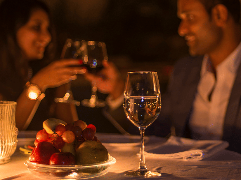 a couple toasting their wine glasses on their romantic candlelight dinner at The Serai, Chikmagalur. It is one of the many experiences in Chikmagalur that the resort provides for couples.