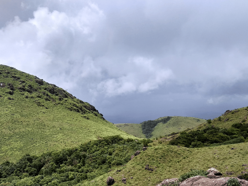 Lush green hills with stormy clouds hovering in the background.