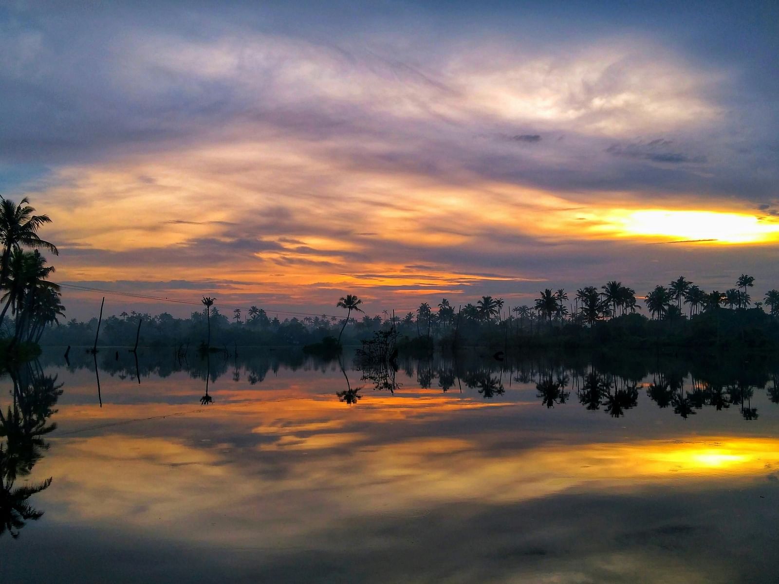A serene sunset reflecting on a calm body of water, lined with trees.