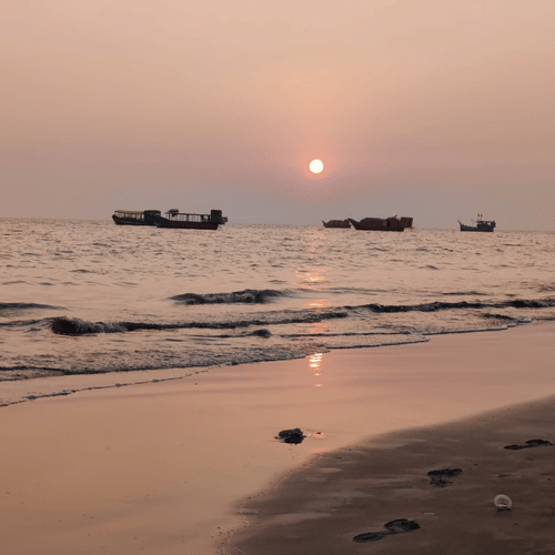 The Balachadi Beach during sunset with a few small boats sailing in the distance.