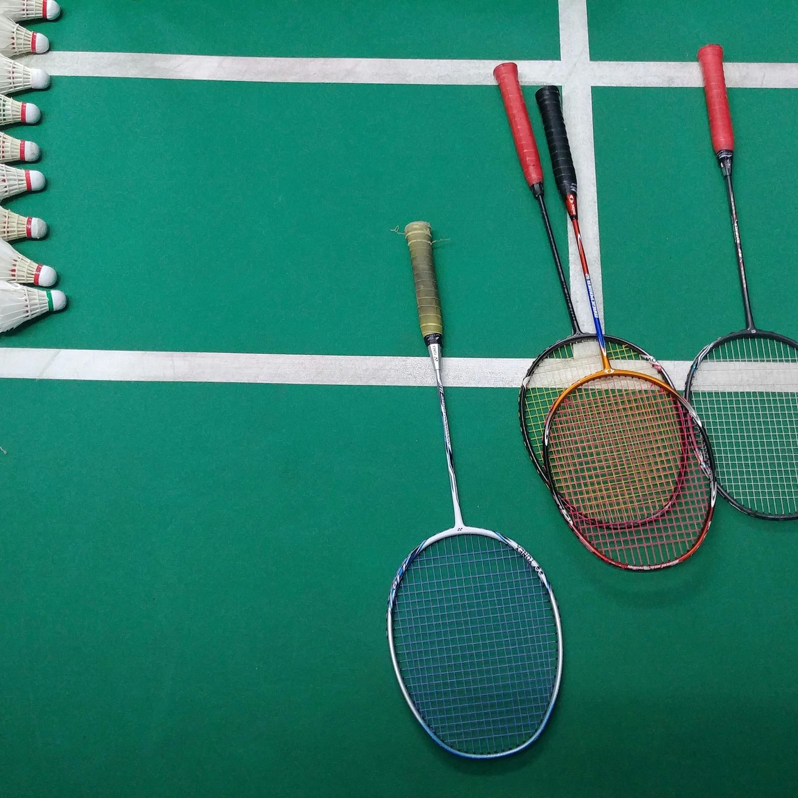 Three badminton rackets and a shuttlecock on a green court.